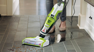 A woman using a vacuum cleaner on a tile floor.