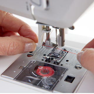 Close-up of hands threading red thread through the needle of a Husqvarna Viking Onyx 15 sewing machine by 38-SVP (Singer Viking Pfaff)—ideal for beginners learning to sew.