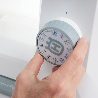 A hand turns the stitch selection dial on the Husqvarna Viking Onyx 15 by 38-SVP (Singer Viking Pfaff), revealing various stitch pattern icons—perfect for beginners exploring creative options.