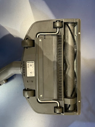 Underside of a Certified Refurbished Sew & Vac Miele C3 Brilliant vacuum cleaner showing the brush roll and wheels on a blue surface.