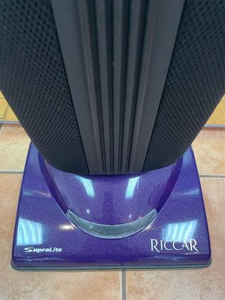 Close-up of the base of a Riccar R10S vacuum cleaner by Sew & Vac in purple with a metal brush roll, standing on a tiled floor.