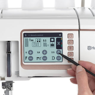 A hand uses a stylus to adjust settings on the touchscreen display of the Sew & Vac Husqvarna Viking Amber Air S600 sewing machine.
