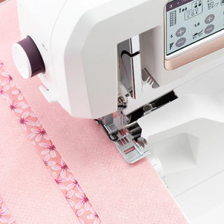 A close-up of the Sew & Vac Husqvarna Viking Amber Air S600 sewing machine stitching decorative patterns on pink fabric.