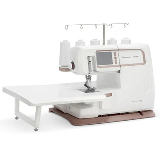 The Sew & Vac Husqvarna Viking Amber Air S600 is a white electronic sewing machine with an extended worktable and four large spools on top, perfect for advanced sewing tasks.