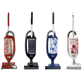 Four Sew & Vac Sebo Felix Premium upright vacuum cleaners with unique patterned covers—red checks, black dots, blue floral, and pink roses—stand in a row on a white background, highlighting their style and multi-surface cleaning versatility.