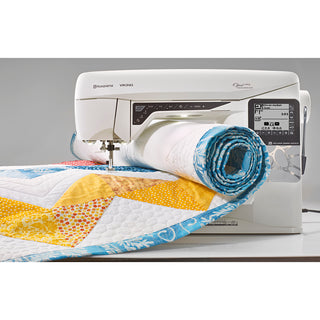 The Husqvarna Viking Opal 690Q expertly sews a colorful quilt with yellow, blue, and orange triangles, highlighting the sewing innovation of Husqvarna Viking.