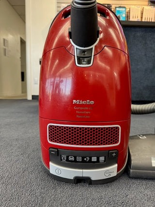 A used Sew & Vac Miele Complete C3 Canister Vacuum with HEPA filtration and a premium power head is placed on a gray carpet in an indoor setting.