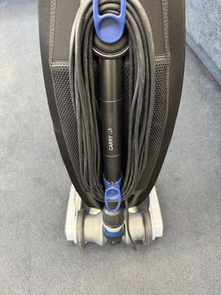 A close-up of the Oreck Magnesium RS Swivel-Steering Upright Vacuum RLW1500RS Certified Reconditioned, a lightweight Oreck model standing on carpet with its power cord neatly wrapped around the hooks.