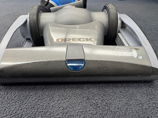 Close-up of the base of an Oreck Magnesium RS Swivel-Steering Upright Vacuum RLW1500RS Certified Reconditioned on a carpeted floor.