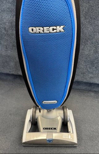 An Oreck Magnesium RS Swivel-Steering Upright Vacuum RLW1500RS Certified Reconditioned stands on a gray carpet, viewed from the front.
