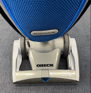 A close-up of the Oreck Magnesium RS Swivel-Steering Upright Vacuum RLW1500RS Certified Reconditioned by Oreck on a gray carpet.