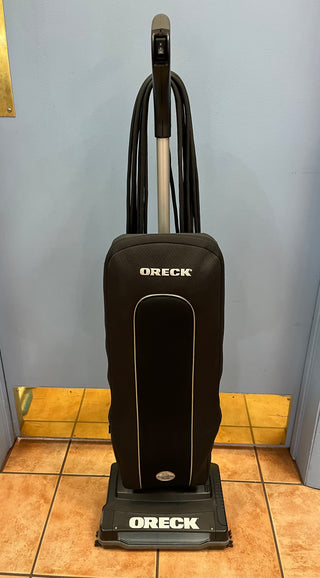 A certified refurbished Sew & Vac Oreck XL21 vacuum cleaner stands on a tiled floor against a blue wall.