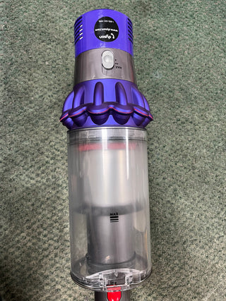 A certified refurbished Sew & Vac Dyson Cyclone v10 Animal handheld vacuum cleaner with a purple top and a clear dust container, placed on a carpeted floor.