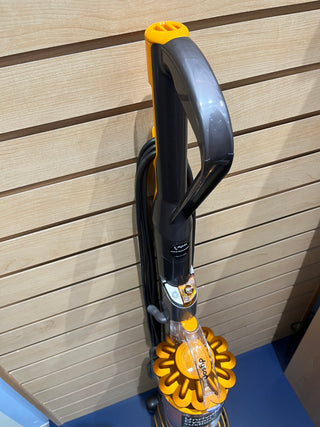 A certified refurbished Sew & Vac Dyson UP19 Multifloor 2 with a gray handle and orange accents is displayed against a wooden slat wall, almost like new.