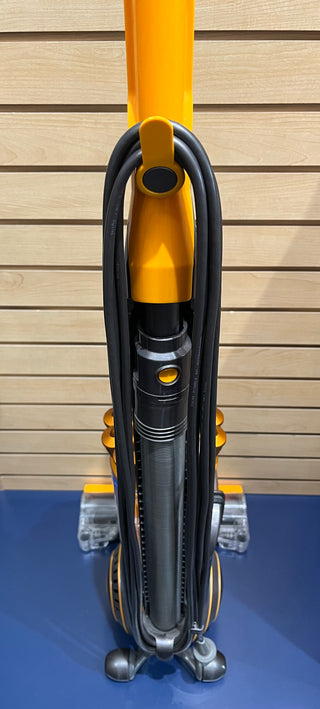 A close-up of a Sew & Vac Dyson UP19 Multifloor 2 with neatly wound cords, placed on a blue surface against a wood-paneled wall, looks almost like new.