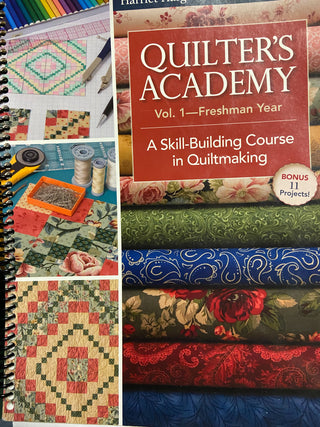 A quilting craft setup including a book titled "Quilter's Academy - Freshman Year," fabric swatches, threads, and a sewing machine on a desk. (Brand Name: Sew & Vac)