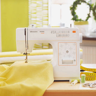 A Husqvarna Viking sewing machine on a table with yellow fabric.