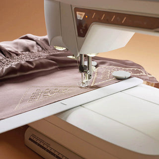 The Husqvarna Viking Designer Topaz 40 by Husqvarna Viking stitches decorative patterns onto light purple fabric with smocked detailing.