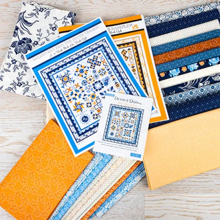 A collection of blue, white, and yellow Denim & Daisies fabric swatches and quilt patterns, including the Halloween Figs Sampler Pattern from the Denim Halloween Figs Quilt Kit featuring Denim & Daisies by Fig Tree Quilts (Moda), laid out on a light wooden surface.