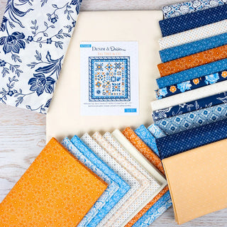 The Denim Halloween Figs Quilt Kit Featuring Denim & Daisies by Fig Tree Quilts from 41-Sew Steady is displayed with blue, orange, and cream fabric squares arranged around the pattern booklet on a white surface.