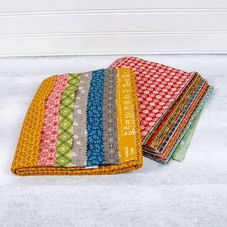 A stack of colorful, patterned fabrics from the Let's Make a Snowman Sew Along Quilt Kit Featuring Home Town Holiday by Lori Holt is arranged on a light gray surface. The collection showcases several distinct designs, including stripes, geometric shapes, and floral motifs. Perfect for creating a beautiful quilt top with guidance from Sew & Vac.