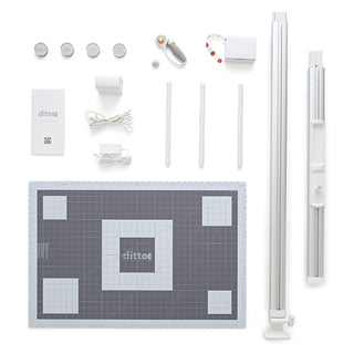 A flat lay of the Singer Ditto Pattern Projector starter kit, featuring a cutting mat, projector parts, rotary cutter, power adapters, cords, and accessories—ideal for making customizable and paperless patterns easily.