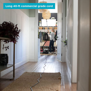 A woman is standing in a hallway, about to buy a Simplicity BRIO Canister vacuum online.