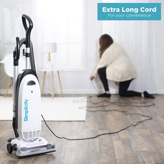 A person in a living room plugs in the simplicity Simplicity S20EZM Allergy Bagged Upright vacuum with an extra-long cord. Text in the corner reads, "Extra Long Cord For your convenience.