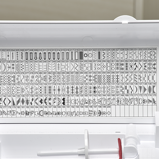 Close-up of the Baby Lock Allegro Quilting and Sewing Machine's stitch guide, displaying numbered built-in basic, decorative, and buttonhole stitches printed inside the lid.