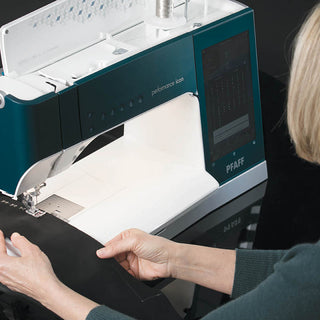 A user guides black fabric under the needle of the PFAFF Performance Icon, utilizing its largest working area for enhanced ease and precision.