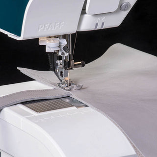Close-up of the PFAFF Performance Icon sewing machine stitching two pieces of light gray fabric, showcasing its needle, presser foot, and industry-leading large workspace for greater control.