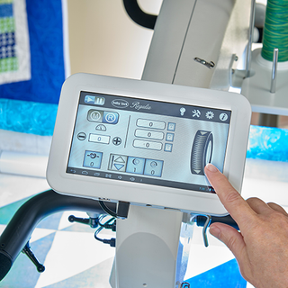 A hand adjusting settings on the digital control panel of a Baby Lock 20" Regalia Stationary Machine with Table and Insert, with a display showing various operational icons including the Stitch Regulator.