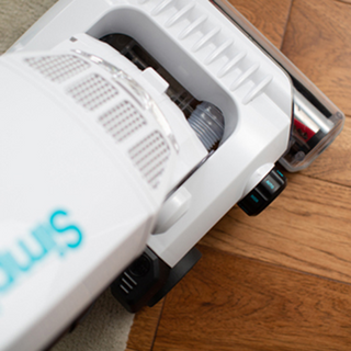 A close-up of the simplicity Simplicity S20EZM Allergy Bagged Upright vacuum with strong suction cleaning a hardwood floor and a light-colored rug.