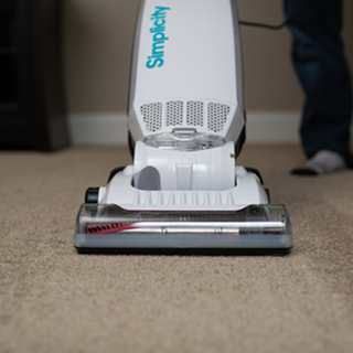 Someone vacuums a beige carpet at home using the Simplicity S20EZM Allergy Bagged Upright by simplicity, featuring powerful suction and HEPA filtration.