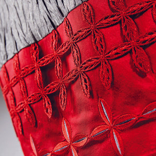Close-up of red fabric featuring intricate geometric embroidery made with PFAFF Creative 3.0 designs, and pleated gray material at the top.