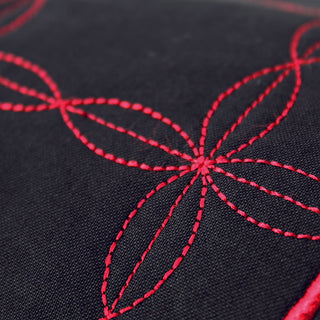Close-up of black fabric shows embroidery with overlapping red ovals forming a geometric floral pattern, created using the Exclusive Stitch Creator on the PFAFF Creative 3.0 sewing machine.