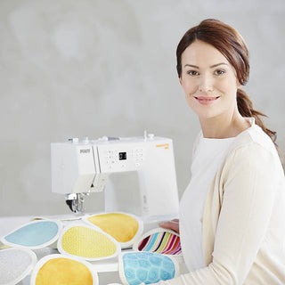 A woman is standing in front of a PFAFF Passport 3.0 sewing machine.