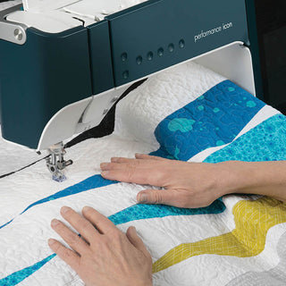 A person guides a colorful quilt under the needle of a PFAFF Performance Icon sewing machine, recognized for its largest working area, while quilting.
