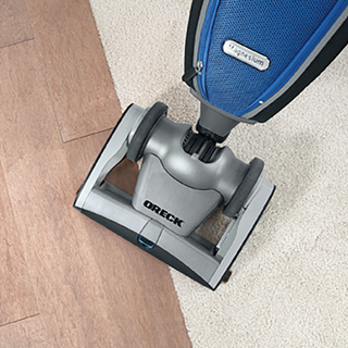 An oreck upright vacuum cleaner being used on a beige carpet.