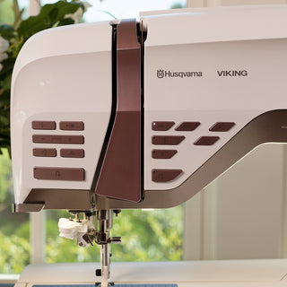 A white and brown Husqvarna Viking sewing machine, the Husqvarna Epic 95Q, is sitting on a table.