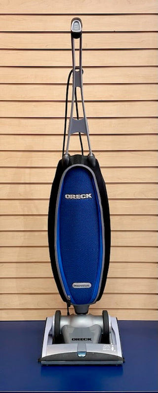 A lightweight Oreck Magnesium LW1500RS vacuum cleaner in good condition sitting on top of a blue wall.