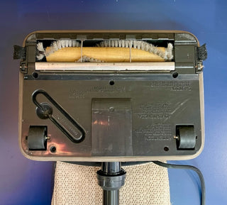 A Sew & Vac Oreck XL - Certified Reconditioned upright vacuum cleaner base displaying its internal brush and components on a blue surface.