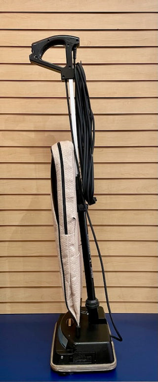 A Sew & Vac Oreck XL - Certified Reconditioned with a black handle and base, wrapped in a black cord and featuring 2 speeds, stands against a blue slatted wall.