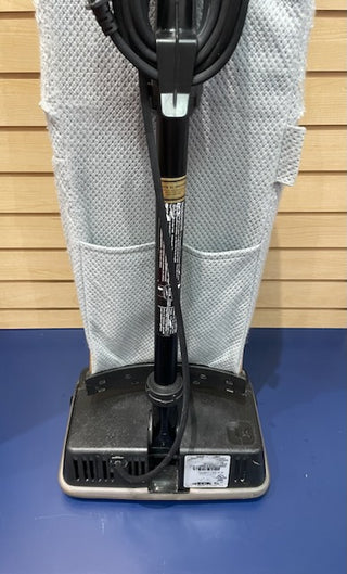 Commercial Oreck XL floor buffer machine, certified refurbished, positioned against a textured white wall with a folded towel, showing the handle, body, and cleaning instructions label.