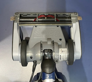 Top view of a Sew & Vac Oreck Magnesium - Certified Refurbished lightweight gray vacuum cleaner head with rollers and brushes visible on a blue surface.