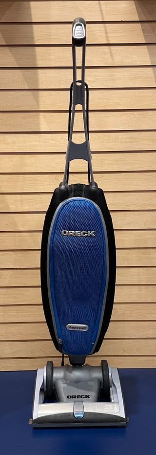 A lightweight, Certified Refurbished Oreck Magnesium vacuum in sleek silver and blue colors sitting on top of a table.