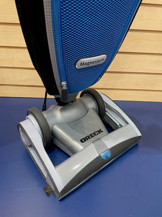 A refurbished blue Oreck Magnesium vacuum on a table in great condition.
