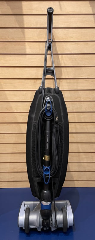 A Certified Refurbished Oreck Magnesium vacuum cleaner perched on a blue wall, featuring like-new parts.