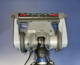 A reconditioned Oreck Magnesium LW1500RS showing its brush roller and wheels against a blue background.