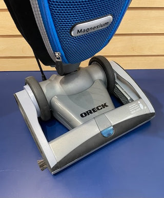A close-up photo of a blue and silver Sew & Vac Certified Refurbished Oreck Magnesium LW1500 vacuum cleaner on a blue surface.